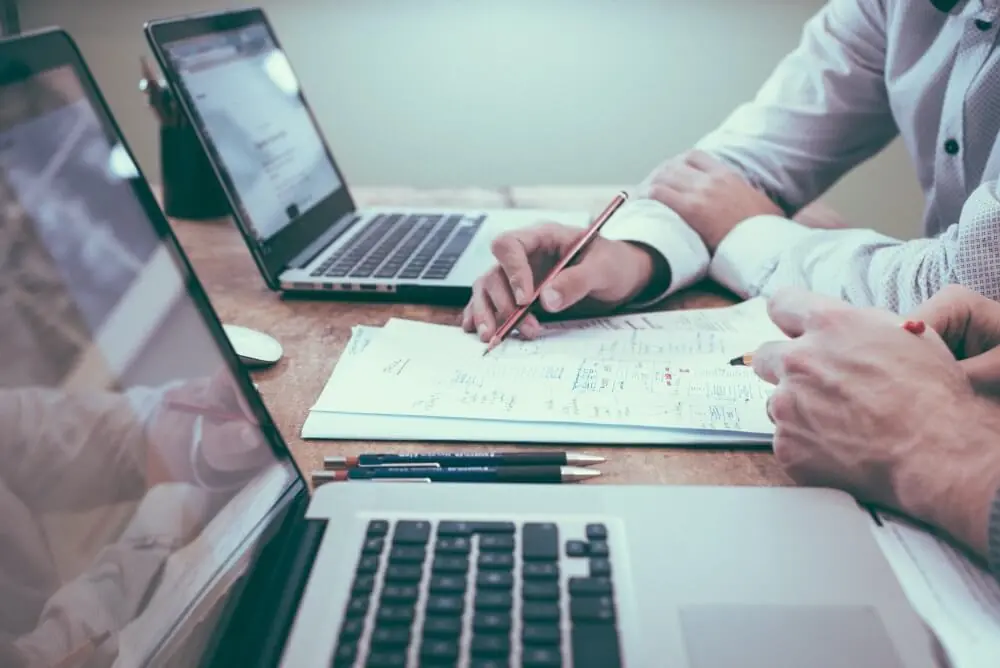 Image of two people collaborating with laptops, paper, and pen