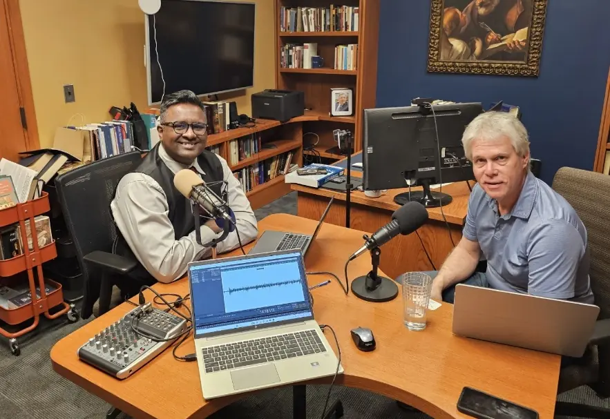 A couple of men sitting at a desk with laptops and microphones AI-generated content may be incorrect.